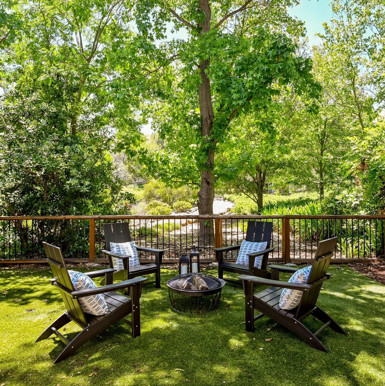 Outdoor chairs around a fire pit beside a deck railing and leafy trees
