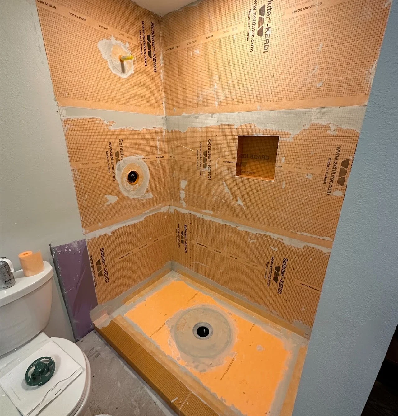 Shower construction with orange waterproofing membrane and an installed shower pan