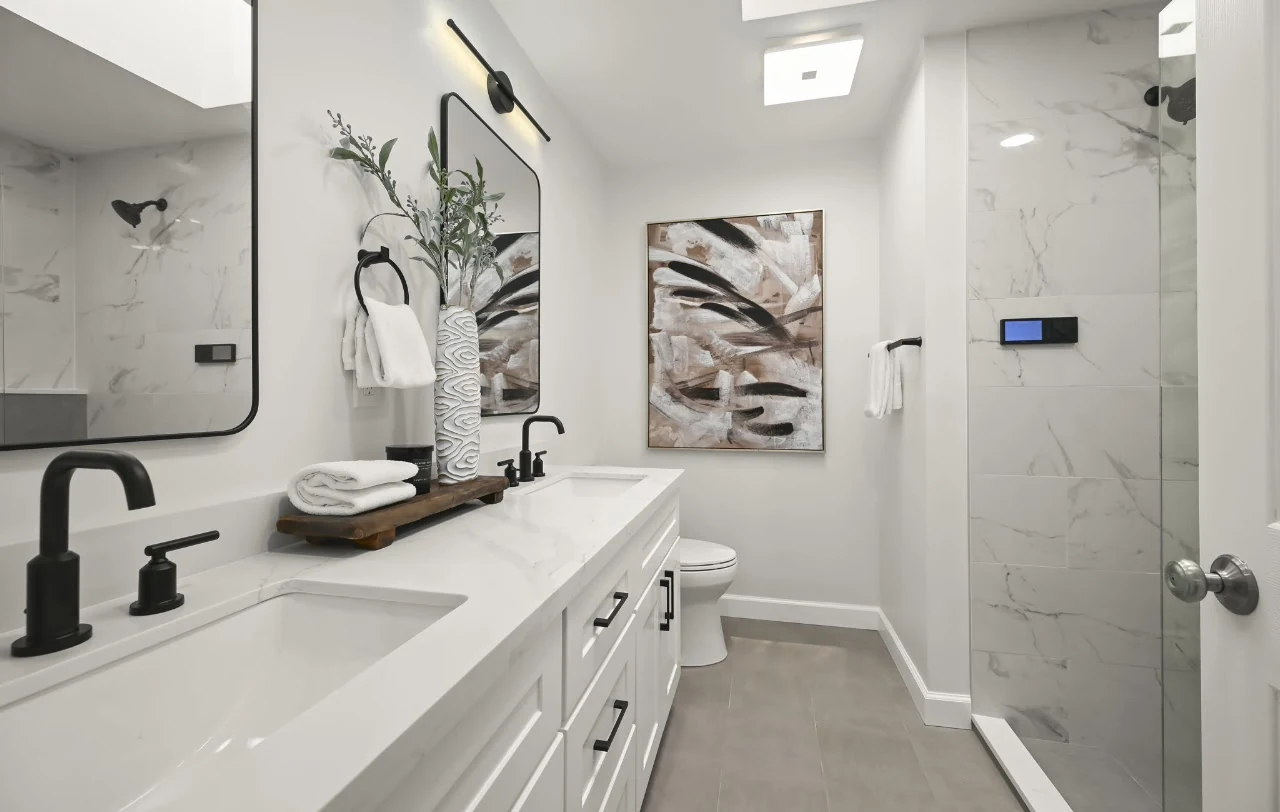 White bathroom vanity with black fixtures beside a glass-enclosed tiled shower