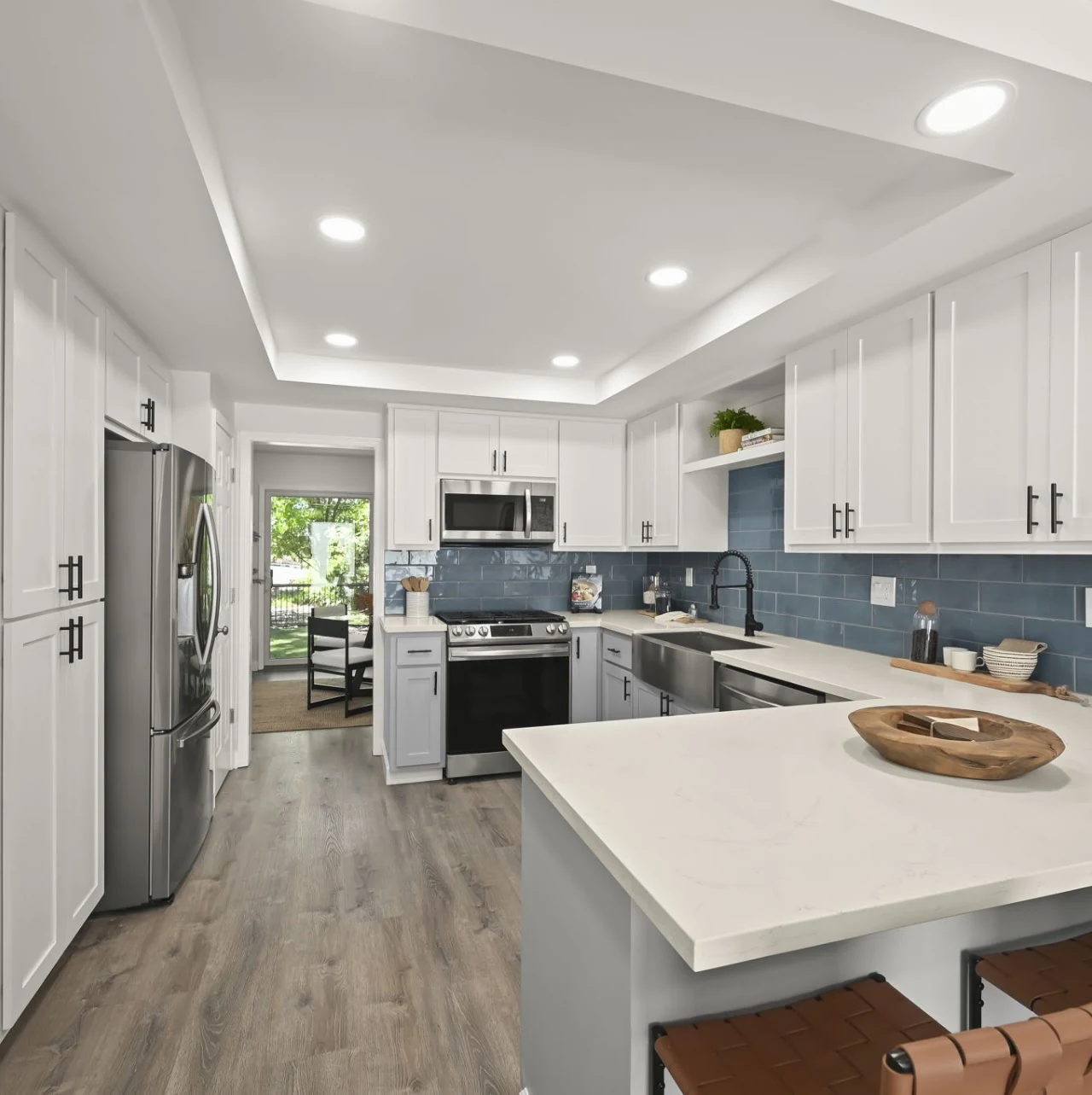 White kitchen with an island, blue tile backsplash and wood-look flooring