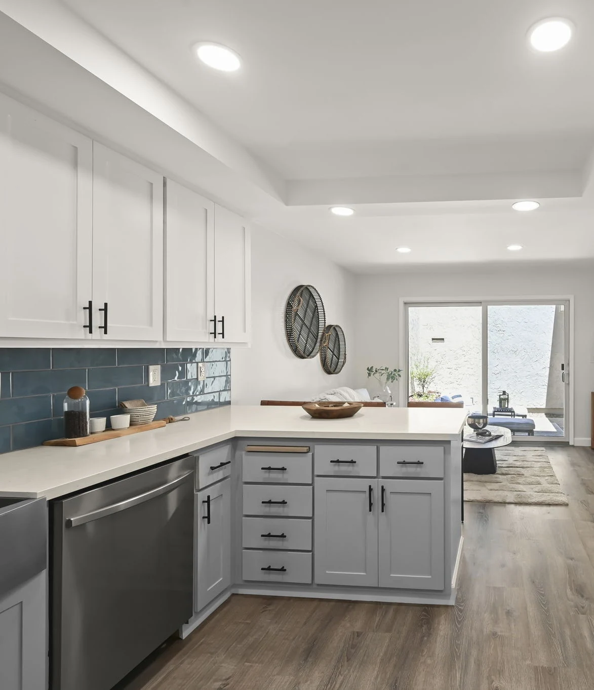 Kitchen view along white cabinets and blue tile backsplash toward a sitting area