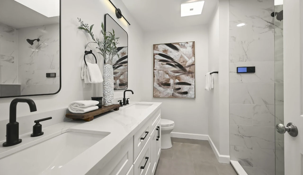 Long white bathroom vanity with black fixtures and a tiled shower