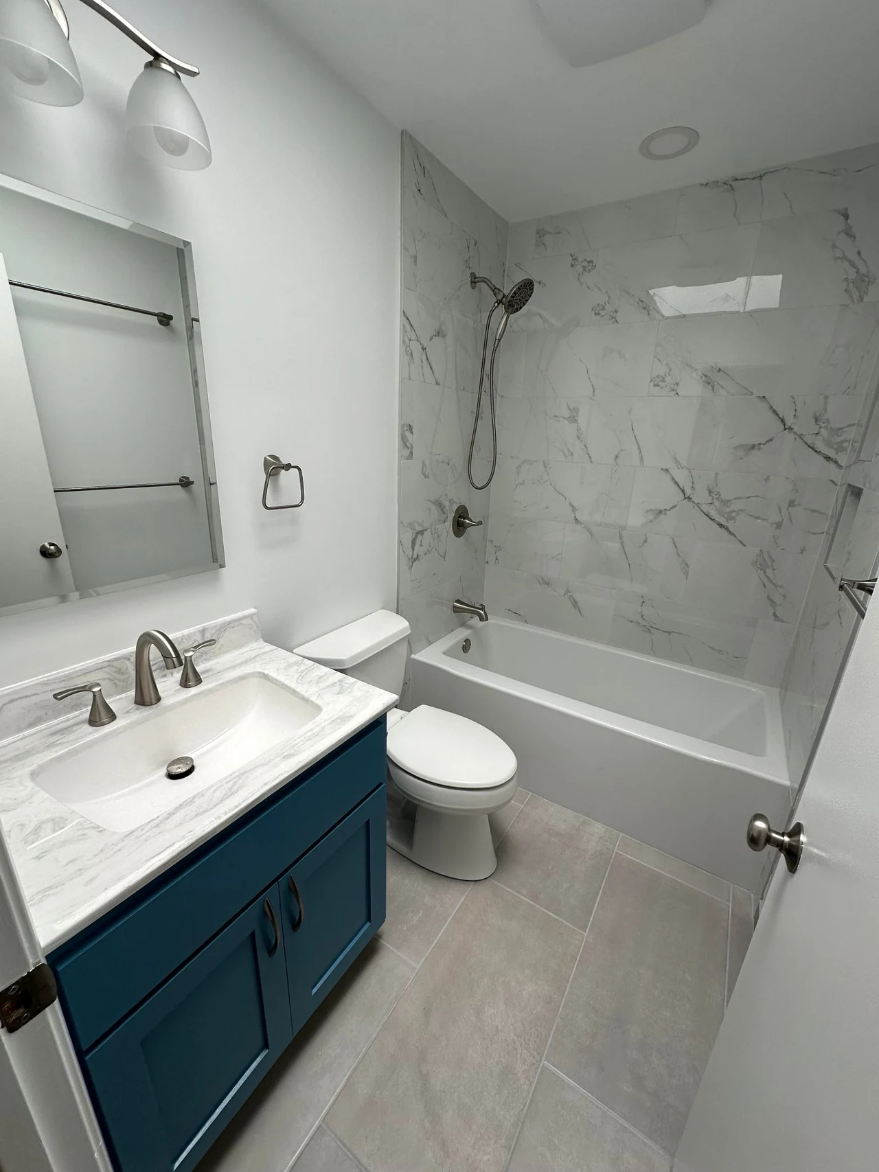 Bathroom with a blue vanity, white countertop and bathtub with tiled surround
